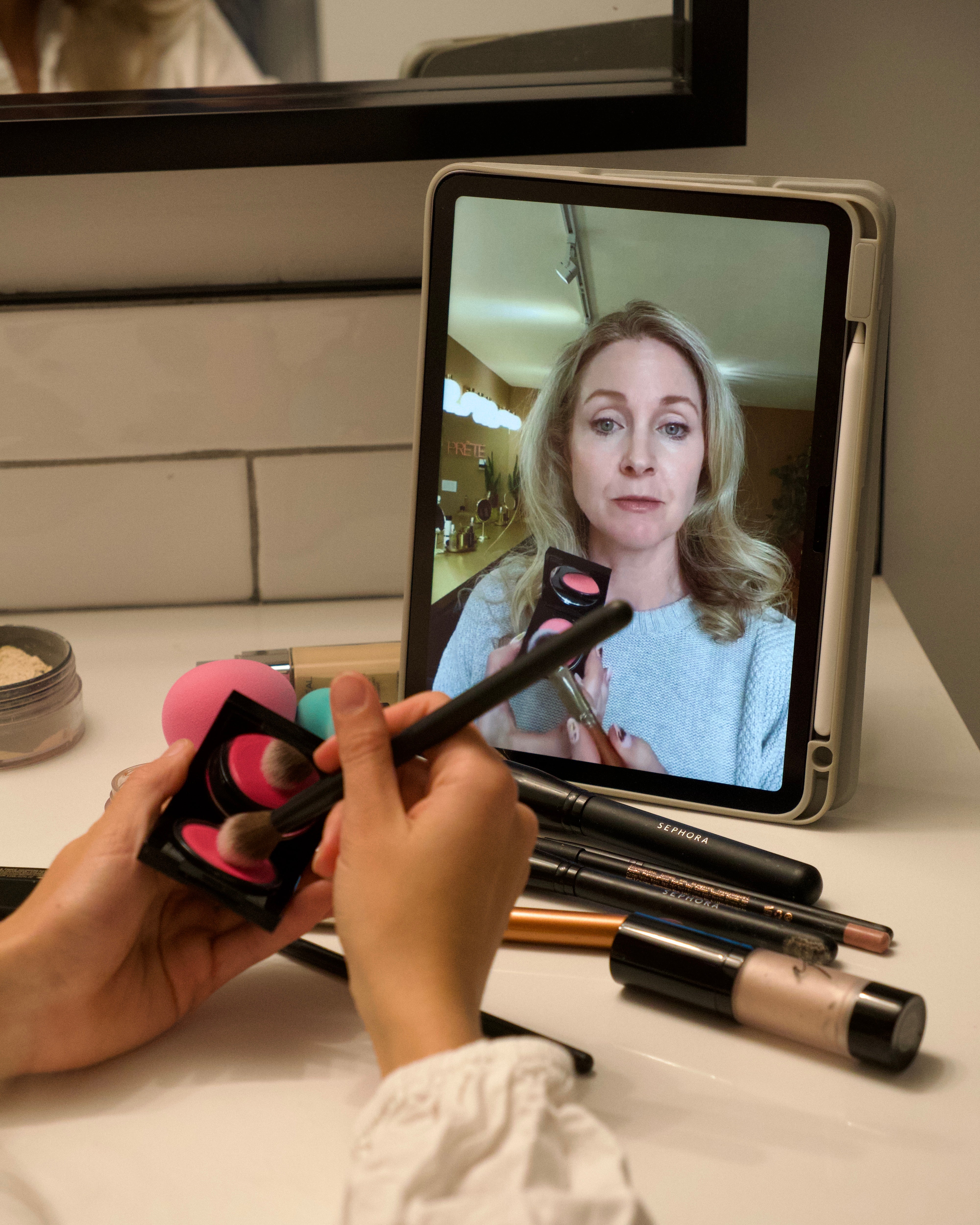 Person using makeup with a tablet showing a basic makeup class online