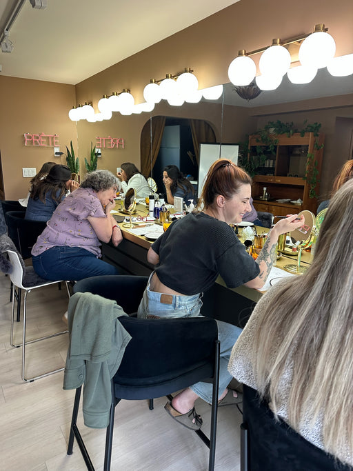 People sitting at a calgary makeup class with mirrors and lights on the wall getting makeup guidance.