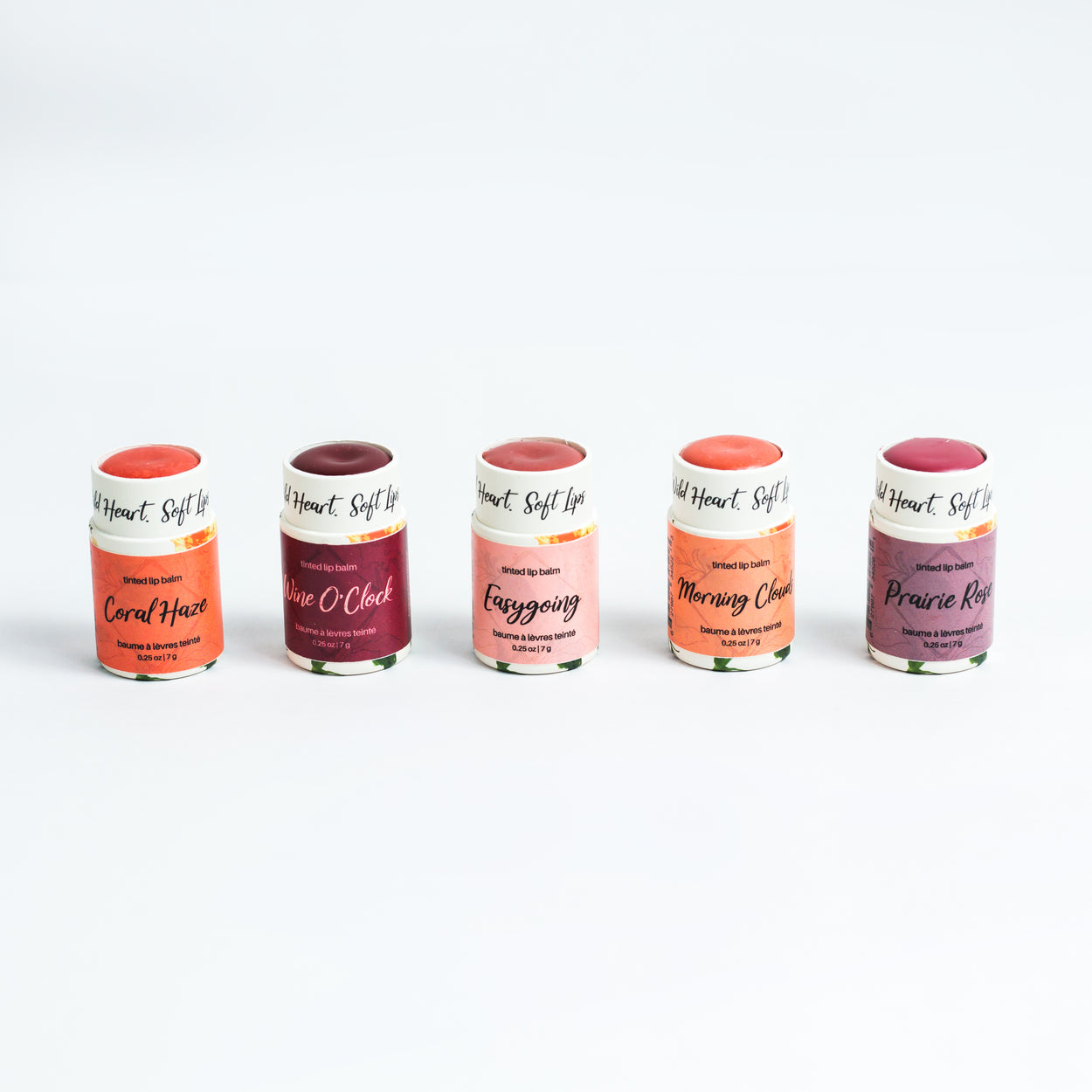 A collection of five tinted lip balms in various colors, with their caps off.